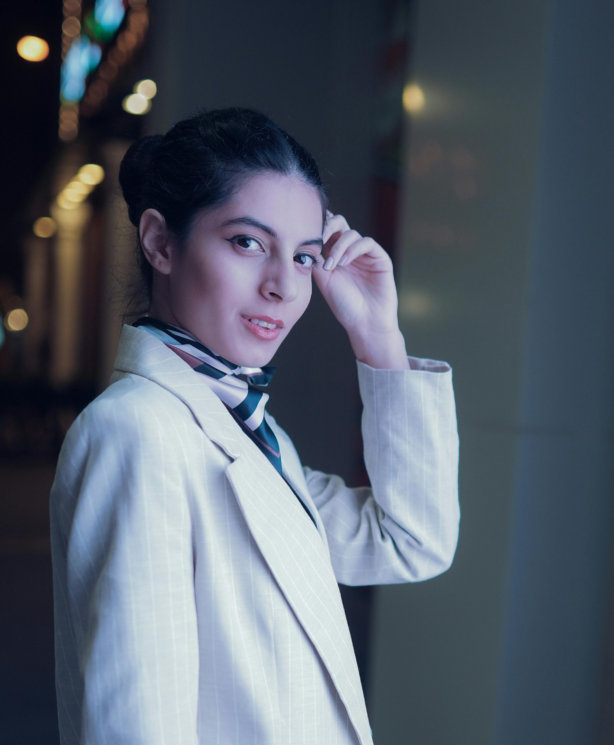 Portrait of a stylish woman in a light suit and scarf, posing outdoors at night in Dubai.