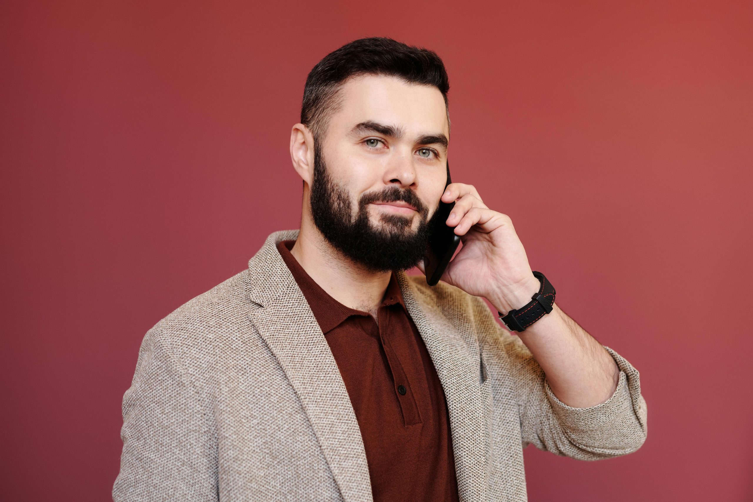 Portrait of a confident businessman with a beard on a phone call, wearing a blazer in a studio shoot.