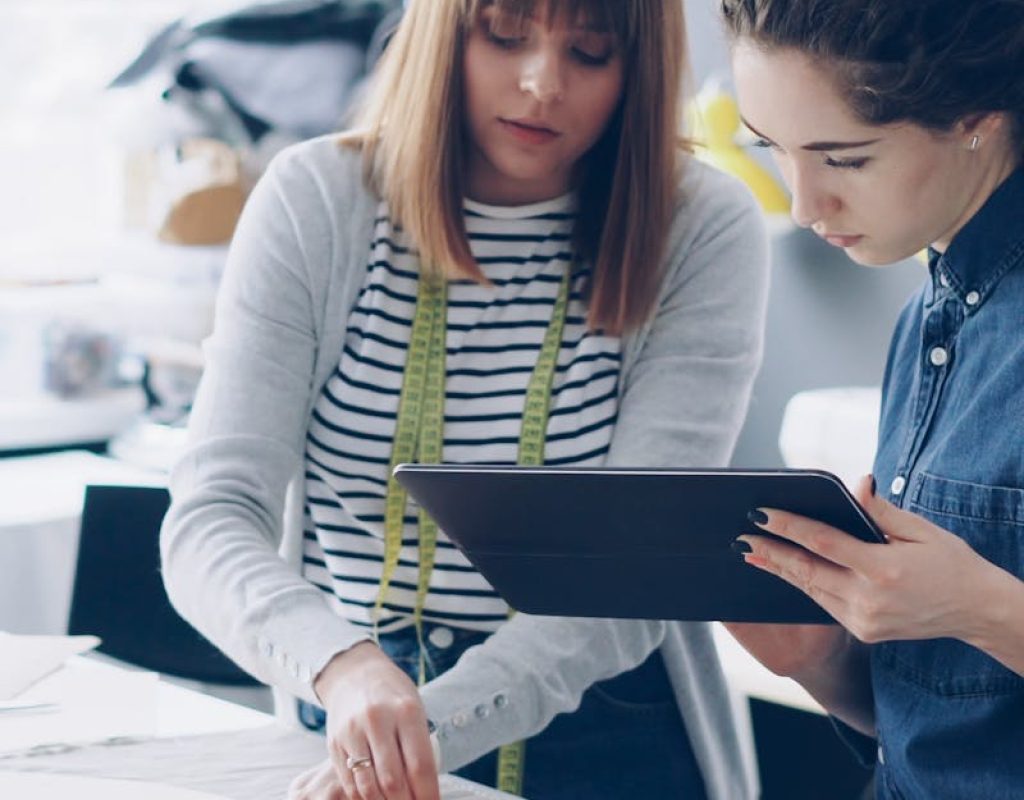 Two female fashion designers working together over fabric patterns in a bright studio.